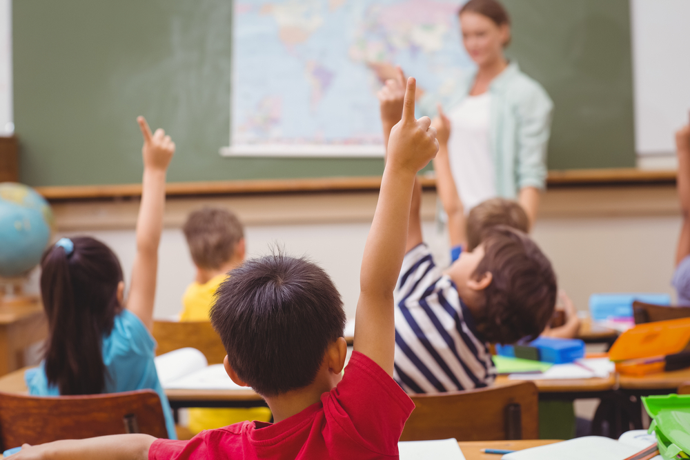 Pupils raising hand during geography lesson in classroom at the elementary school